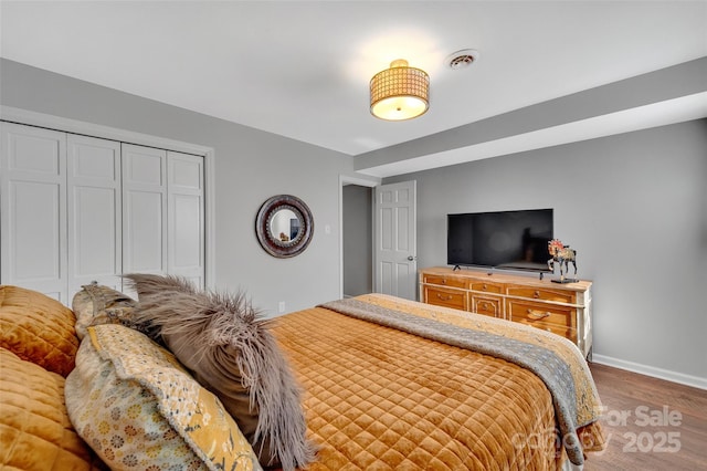 bedroom with wood finished floors, visible vents, a closet, and baseboards