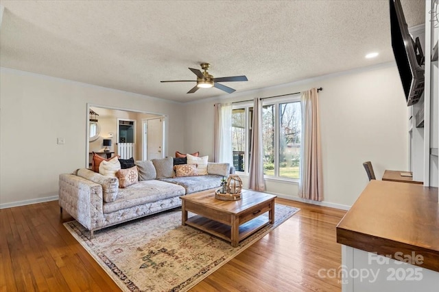 living room featuring ornamental molding, a textured ceiling, light wood finished floors, baseboards, and ceiling fan