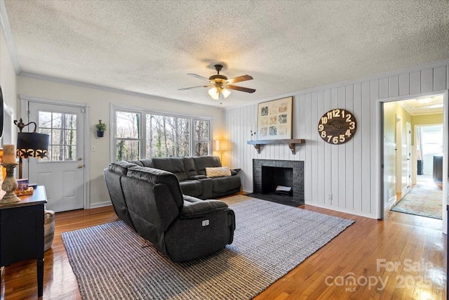 living room with a textured ceiling, a brick fireplace, wood finished floors, and ornamental molding