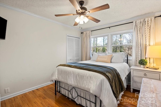 bedroom with baseboards, ornamental molding, wood finished floors, a closet, and a textured ceiling