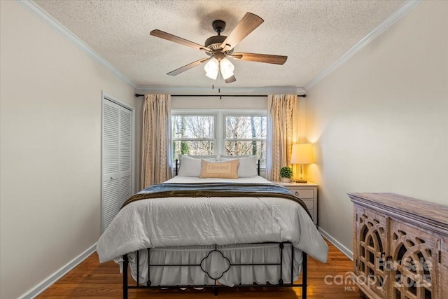 bedroom with a closet, baseboards, wood finished floors, and crown molding