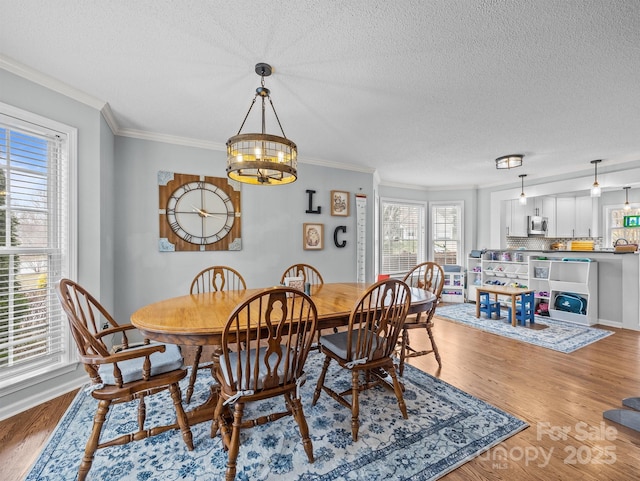 dining space featuring a textured ceiling, crown molding, wood finished floors, and a chandelier