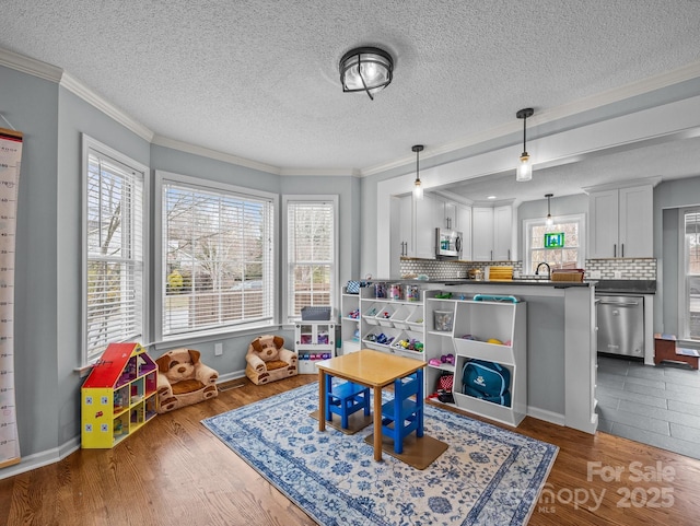 game room with crown molding, wood finished floors, baseboards, and a sink