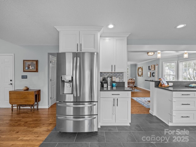 kitchen featuring dark wood-type flooring, white cabinetry, dark countertops, stainless steel fridge, and backsplash