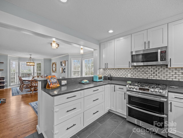 kitchen with backsplash, appliances with stainless steel finishes, a peninsula, and white cabinetry