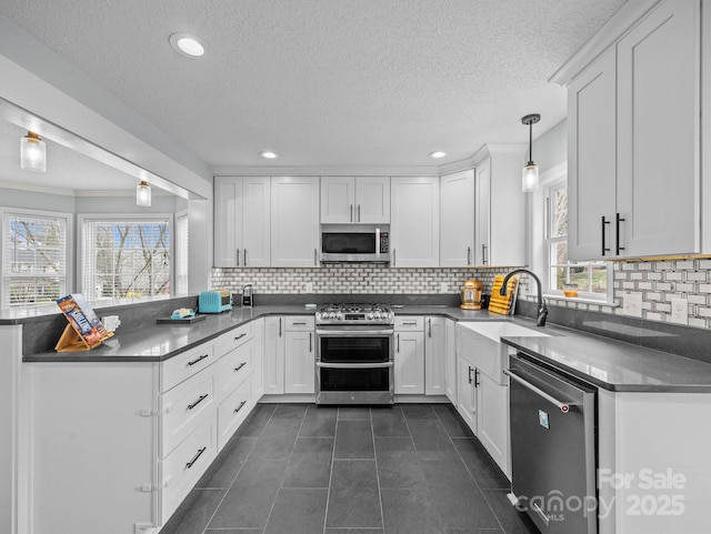 kitchen with a peninsula, a sink, stainless steel appliances, white cabinets, and dark tile patterned floors