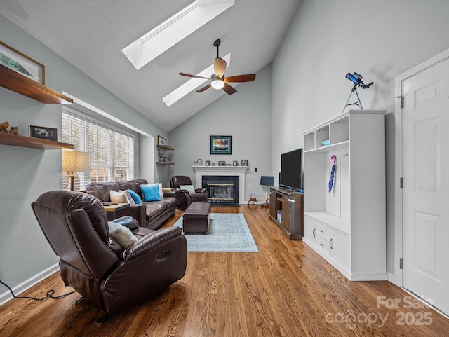 living area with a fireplace with flush hearth, a ceiling fan, wood finished floors, a skylight, and baseboards