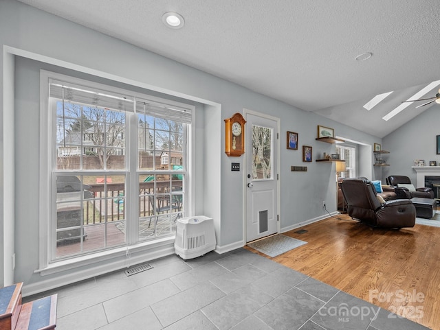 foyer featuring lofted ceiling with skylight, a textured ceiling, baseboards, and wood finished floors