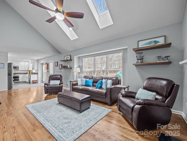 living area with baseboards, a skylight, light wood-style floors, and ceiling fan