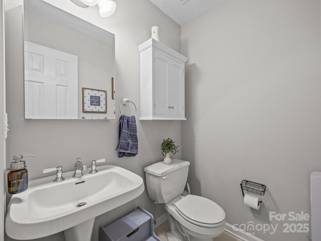 half bath with toilet, baseboards, and a sink