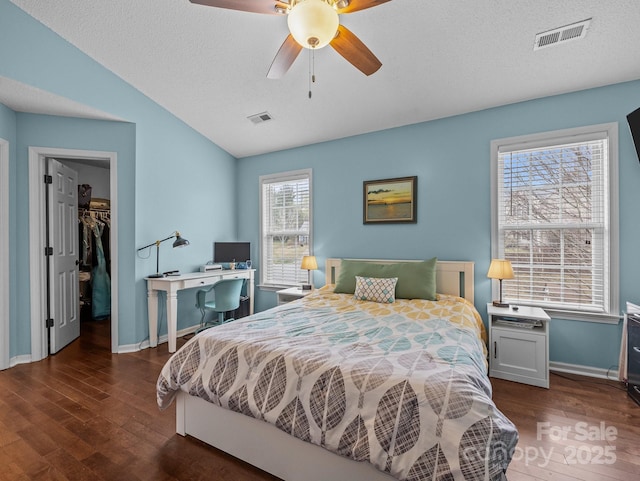 bedroom with visible vents, a walk in closet, lofted ceiling, and wood finished floors