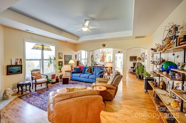 living room featuring a raised ceiling, decorative columns, visible vents, and arched walkways