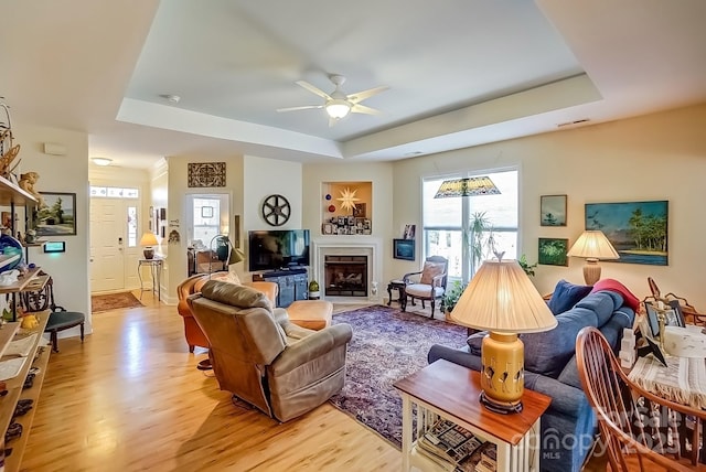 living area with a fireplace with flush hearth, visible vents, a raised ceiling, and light wood-style floors