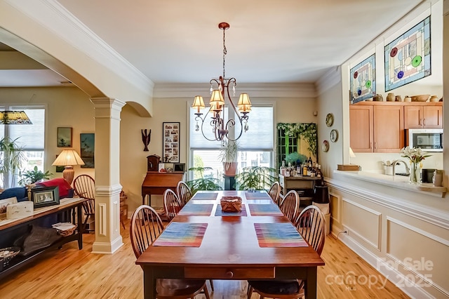 dining space with light wood finished floors, ornate columns, arched walkways, crown molding, and a chandelier