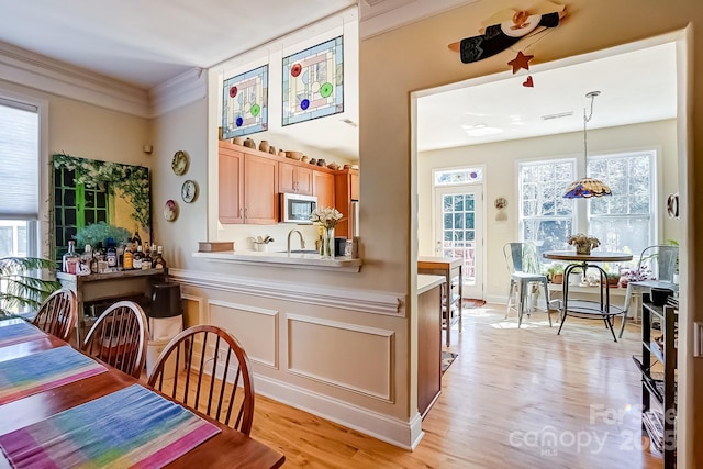 dining space with a healthy amount of sunlight, light wood-style floors, and ornamental molding