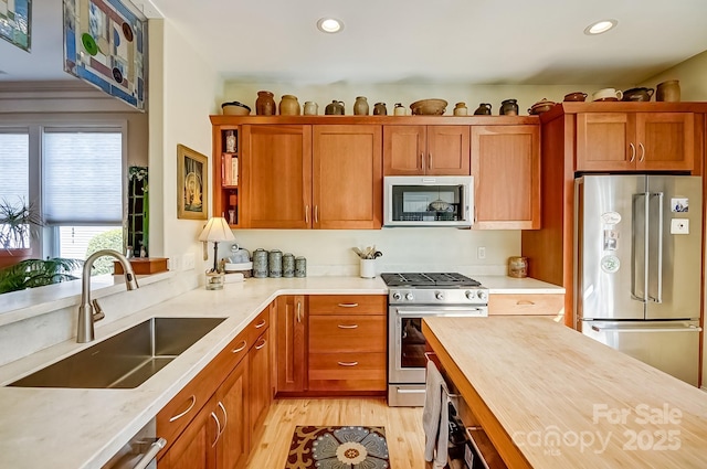 kitchen featuring light wood-type flooring, brown cabinets, a sink, recessed lighting, and appliances with stainless steel finishes