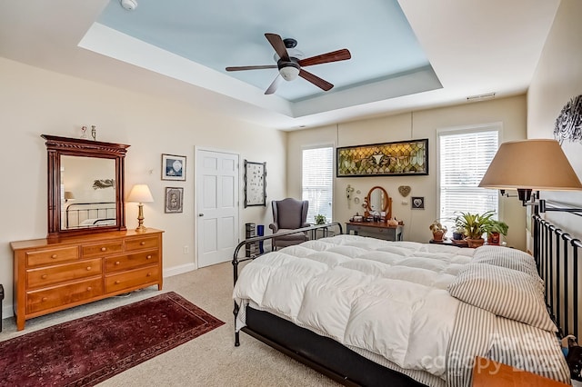 bedroom featuring a ceiling fan, carpet, visible vents, baseboards, and a tray ceiling