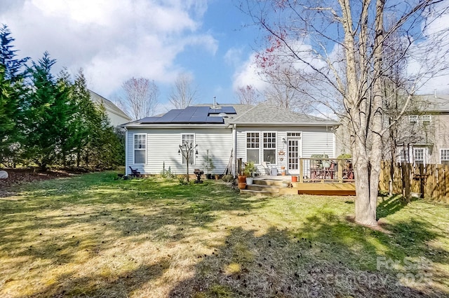 rear view of property featuring solar panels, a wooden deck, and a yard