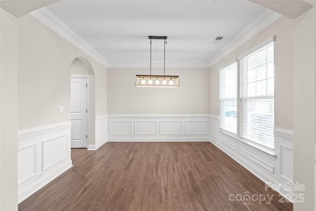 unfurnished dining area with dark wood-style floors, visible vents, arched walkways, wainscoting, and crown molding