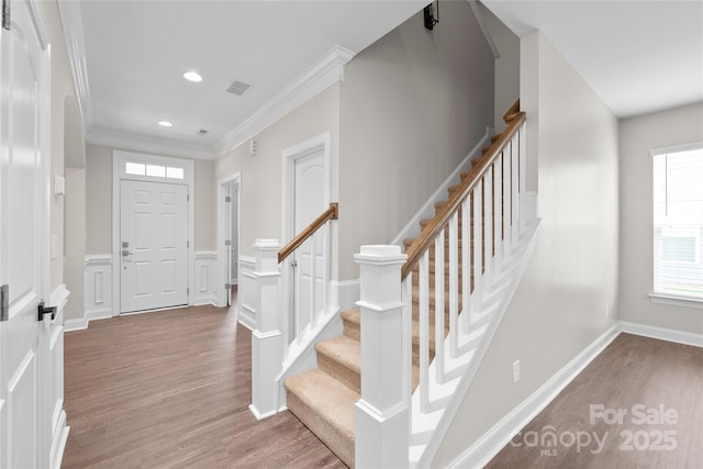 foyer entrance featuring crown molding, a wainscoted wall, stairs, wood finished floors, and a decorative wall