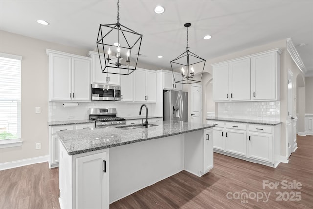 kitchen featuring an island with sink, arched walkways, a sink, stainless steel appliances, and a chandelier