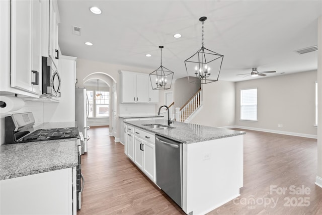 kitchen featuring light wood finished floors, arched walkways, a sink, appliances with stainless steel finishes, and ceiling fan with notable chandelier