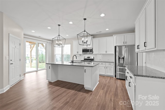 kitchen featuring wood finished floors, a sink, appliances with stainless steel finishes, white cabinetry, and a notable chandelier