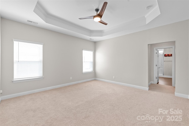 spare room with a tray ceiling, crown molding, visible vents, and light carpet