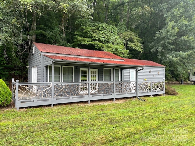 view of front facade featuring metal roof, a view of trees, a porch, and a front lawn