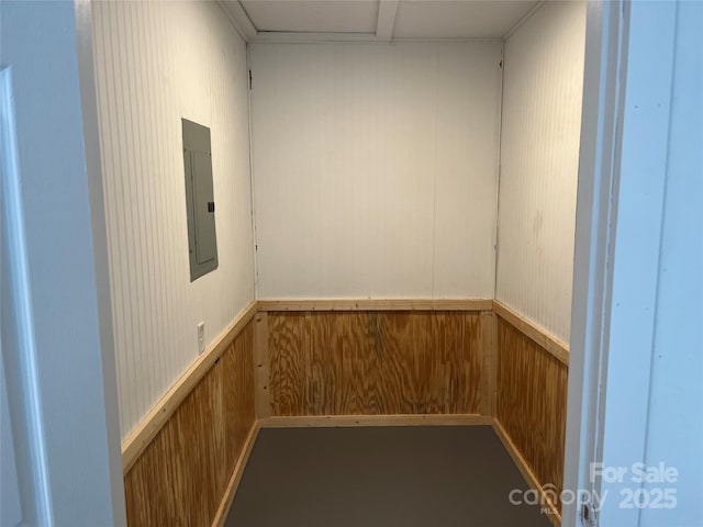 empty room featuring electric panel, wooden walls, elevator, and a wainscoted wall