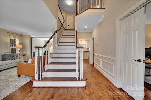 stairs featuring wood finished floors, ornamental molding, wainscoting, and a decorative wall