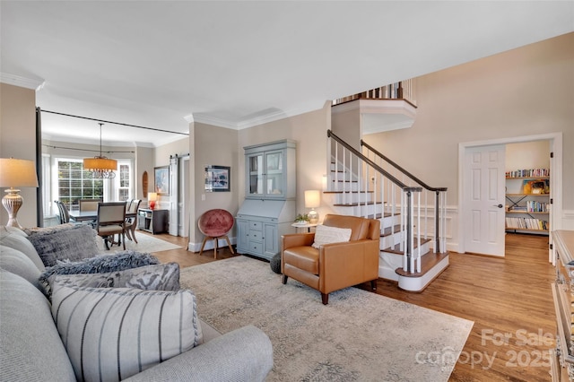 living area featuring stairway, a wainscoted wall, light wood finished floors, and ornamental molding