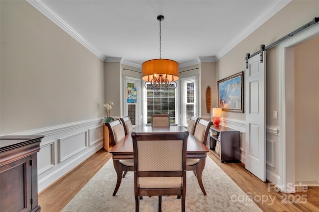 dining room with light wood-style floors, a barn door, and ornamental molding