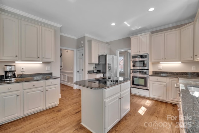 kitchen with dark stone countertops, light wood finished floors, ornamental molding, stainless steel appliances, and white cabinets