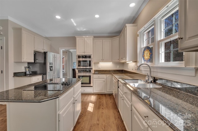 kitchen with a kitchen island, ornamental molding, light wood-style flooring, stainless steel appliances, and a sink