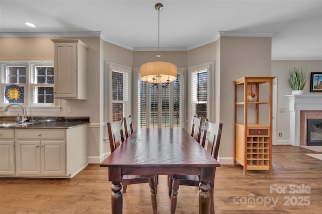 dining space featuring baseboards, a fireplace, light wood-type flooring, and ornamental molding