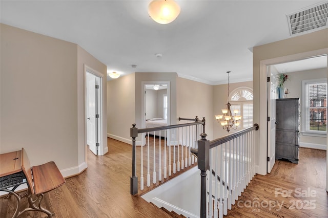 hall featuring visible vents, baseboards, an upstairs landing, an inviting chandelier, and wood finished floors