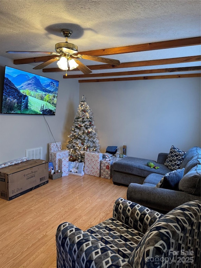 living area featuring wood finished floors, visible vents, ceiling fan, a textured ceiling, and beamed ceiling