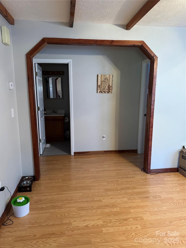 corridor featuring light wood-type flooring, beamed ceiling, and a textured ceiling