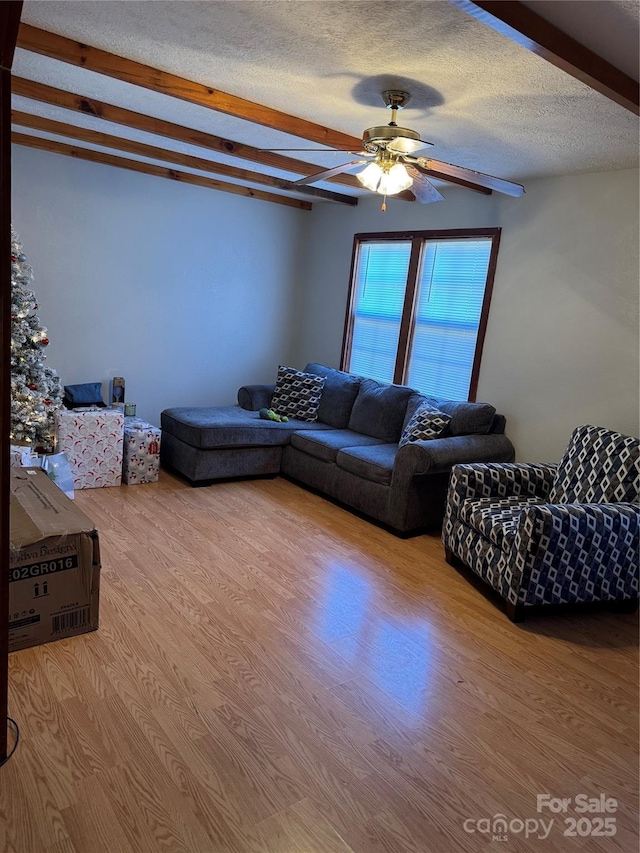 living room with beam ceiling, a textured ceiling, a ceiling fan, and wood finished floors