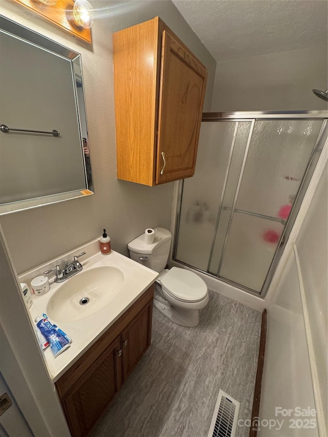 bathroom with vanity, wood finished floors, a shower with shower door, visible vents, and a textured ceiling