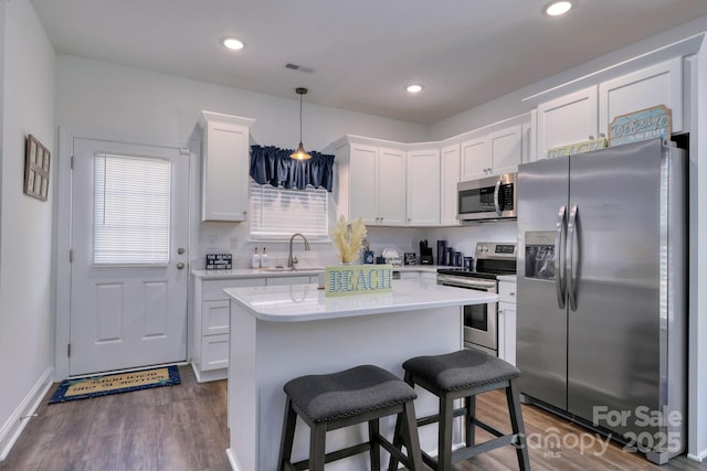 kitchen with a kitchen island, a sink, stainless steel appliances, light countertops, and white cabinetry