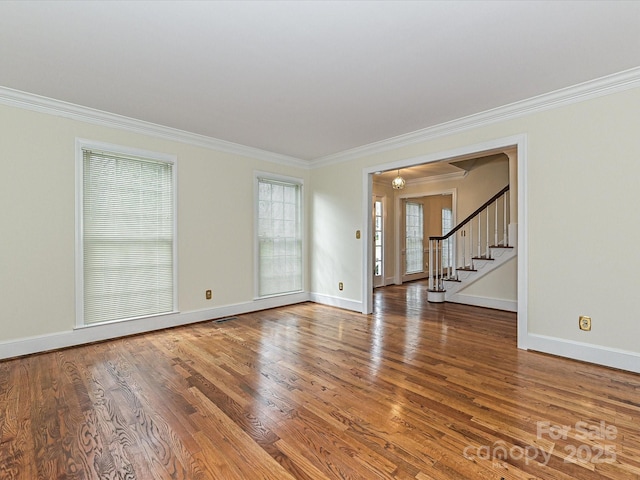 unfurnished room with stairway, wood finished floors, visible vents, baseboards, and ornamental molding