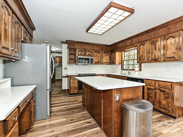 kitchen with a sink, a kitchen island, wood finished floors, appliances with stainless steel finishes, and decorative backsplash