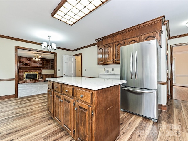 kitchen featuring freestanding refrigerator, crown molding, ceiling fan with notable chandelier, light wood-type flooring, and a center island