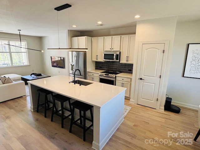 kitchen with a breakfast bar, a sink, decorative backsplash, stainless steel appliances, and light wood-style floors