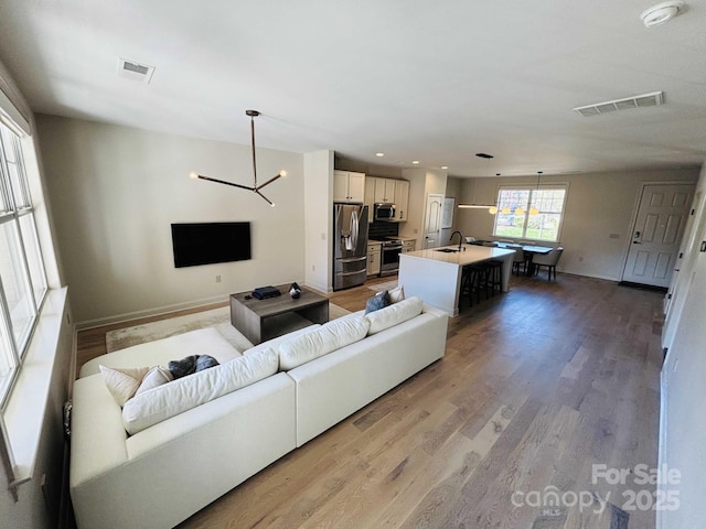 living area with visible vents, baseboards, a chandelier, and light wood finished floors