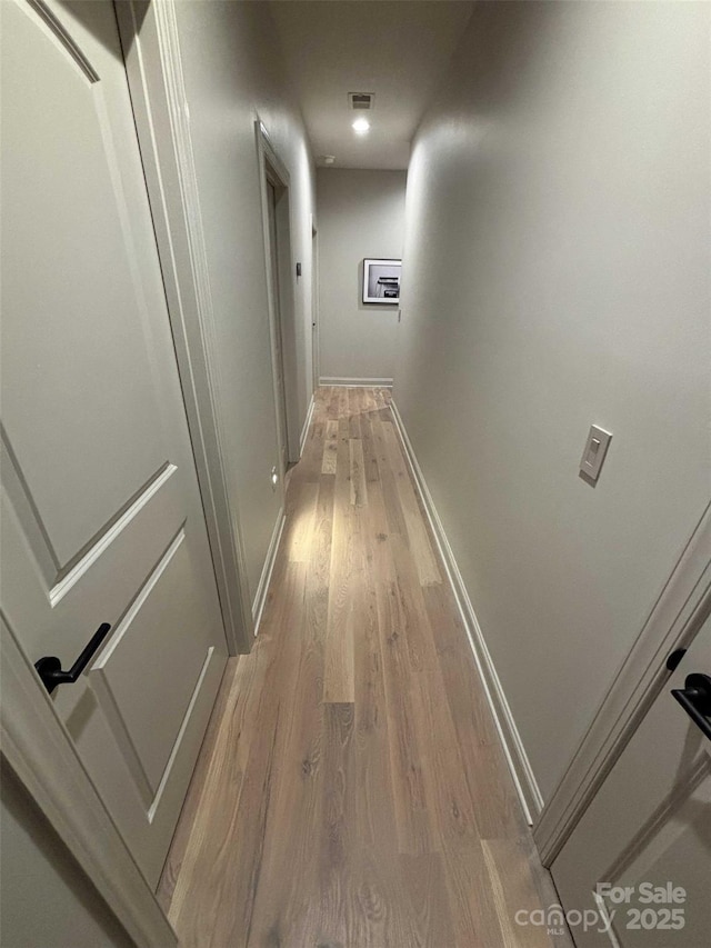 hallway with visible vents, baseboards, and light wood-style floors