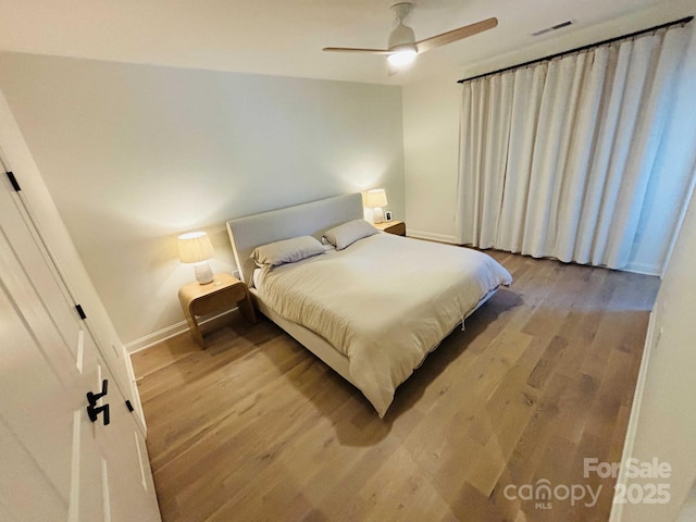 bedroom with visible vents, baseboards, wood finished floors, and a ceiling fan