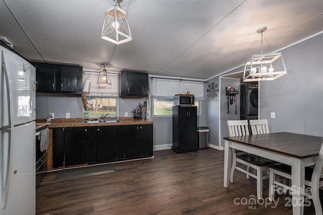 kitchen with dark wood-type flooring, stacked washer and dryer, stainless steel microwave, freestanding refrigerator, and dark cabinets